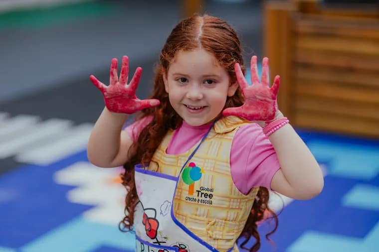 Criança da pré-escola mostrando as mãos pintadas em uma atividade artística